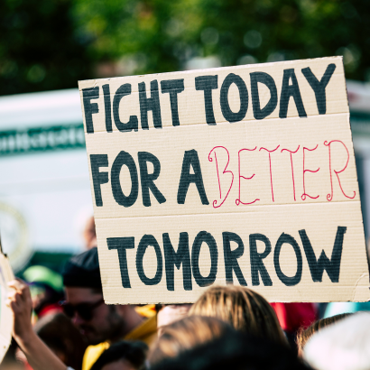 Handwritten protest sign reading "Fight today for a better tomorrow" held above a crowd at an outdoor rally.