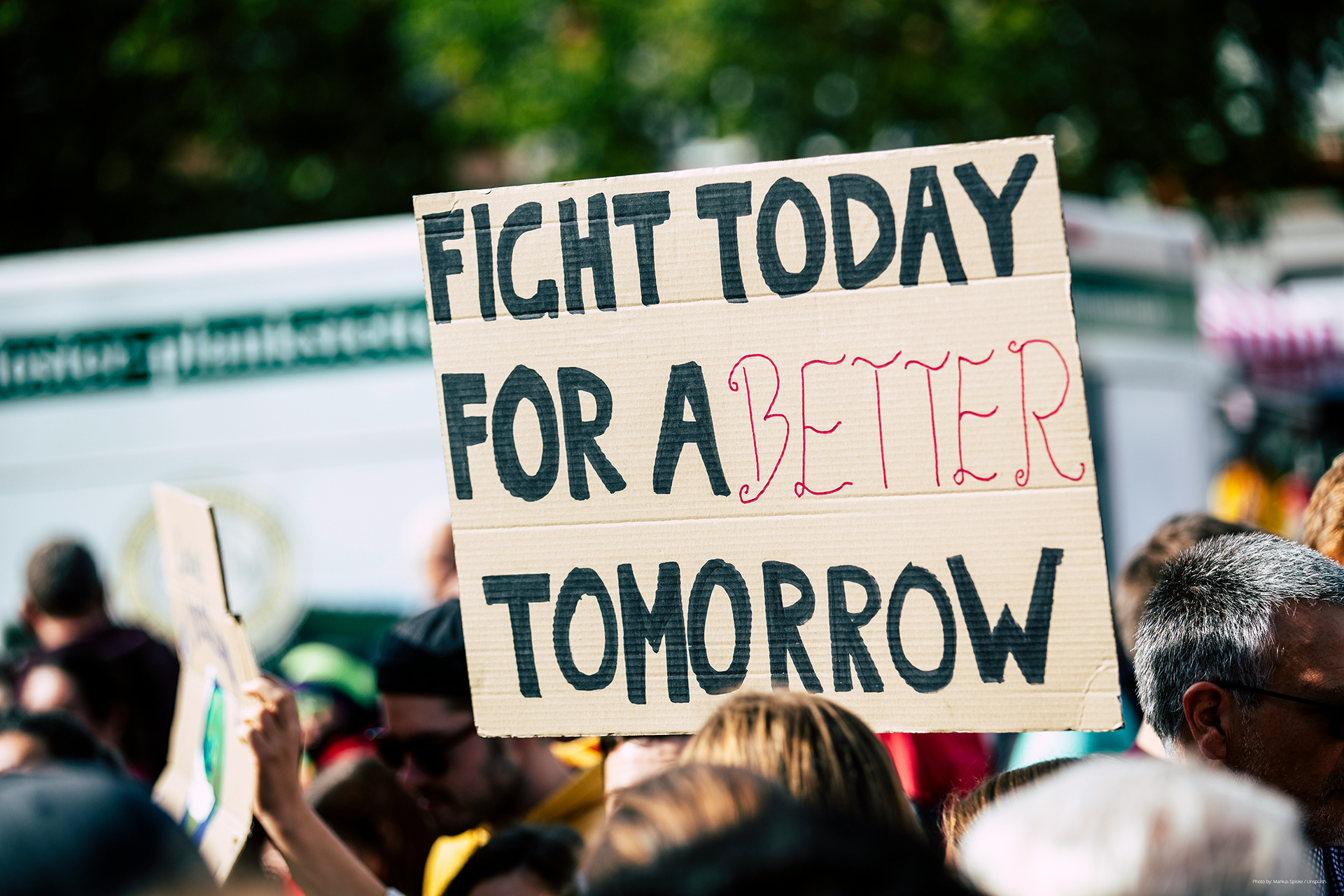 Handwritten protest sign reading "Fight today for a better tomorrow" held above a crowd at an outdoor rally.